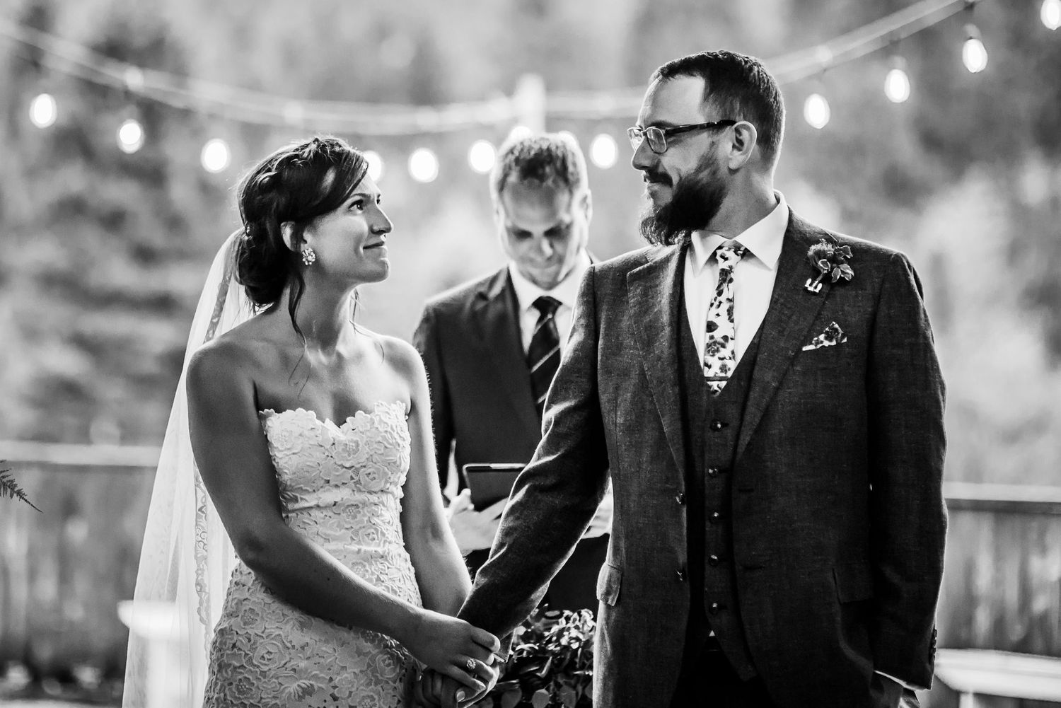Black and white wedding ceremony photo with string lights in background.