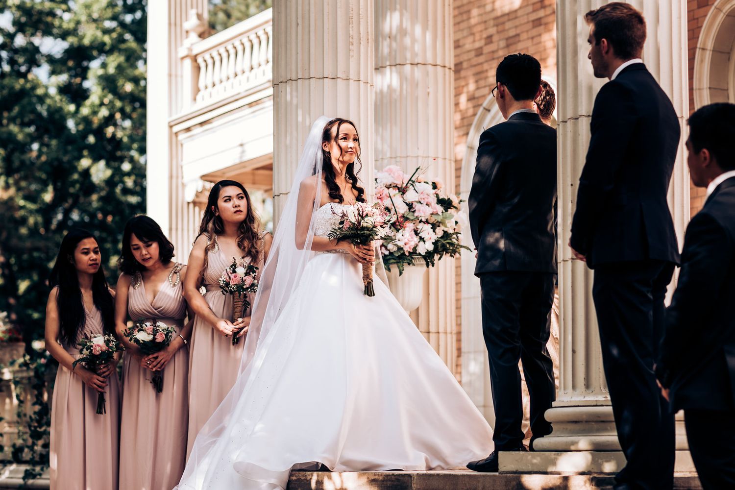 Wedding ceremony takes place on elegant stone steps with bridesmaids in pink dresses.