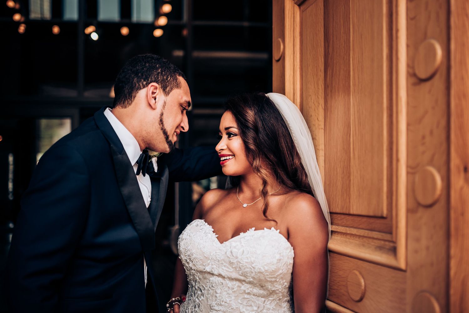 An intimate wedding portrait showing couple sharing tender moment by ornate wooden doors.