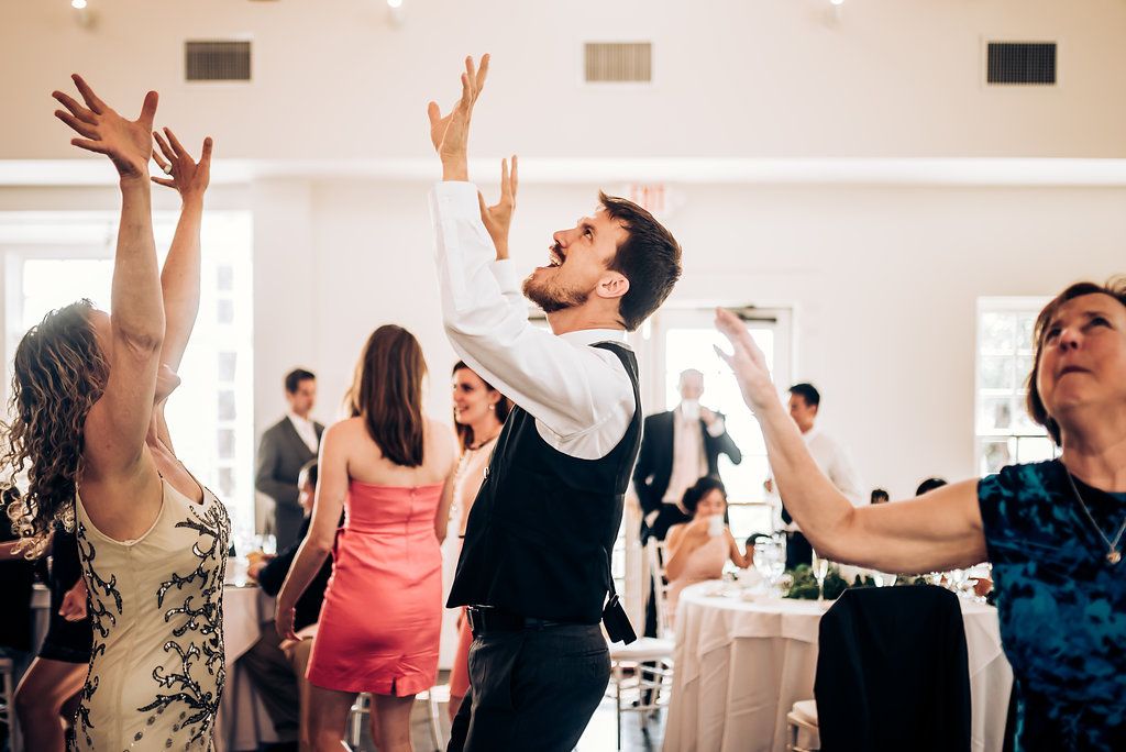 Enthusiastic wedding guests dancing with raised arms on the reception dance floor.