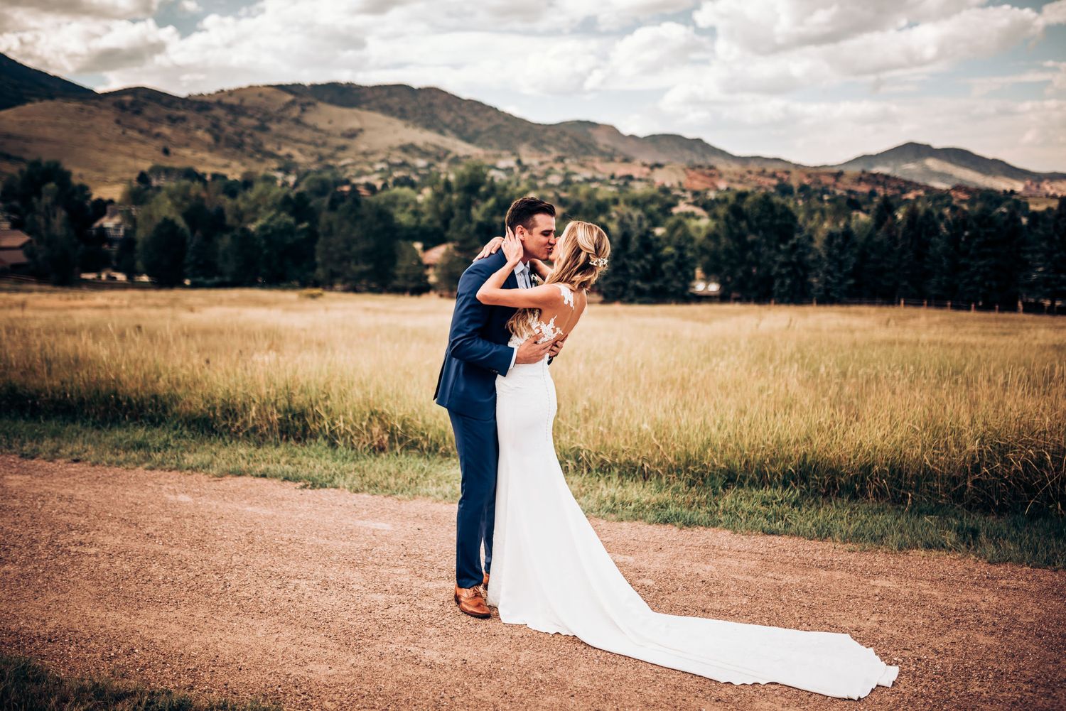 Newlyweds embrace on rustic mountain trail surrounded by golden fields and rolling hills.