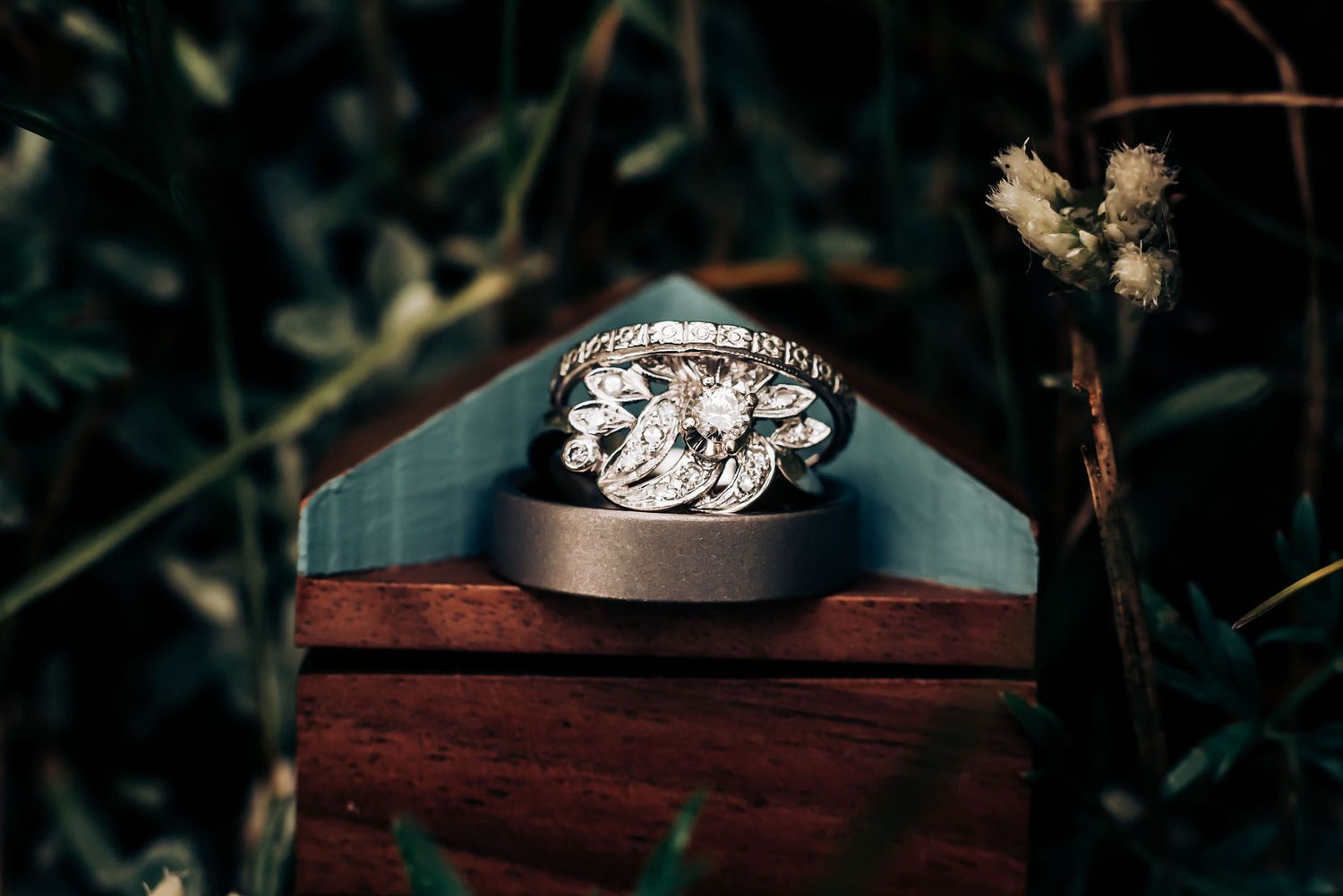Close up of sparkling diamond ring on wooden display box against dark foliage.