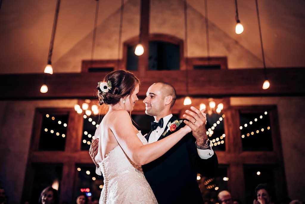 Romantic first dance moment captured under warm lighting in rustic reception venue.