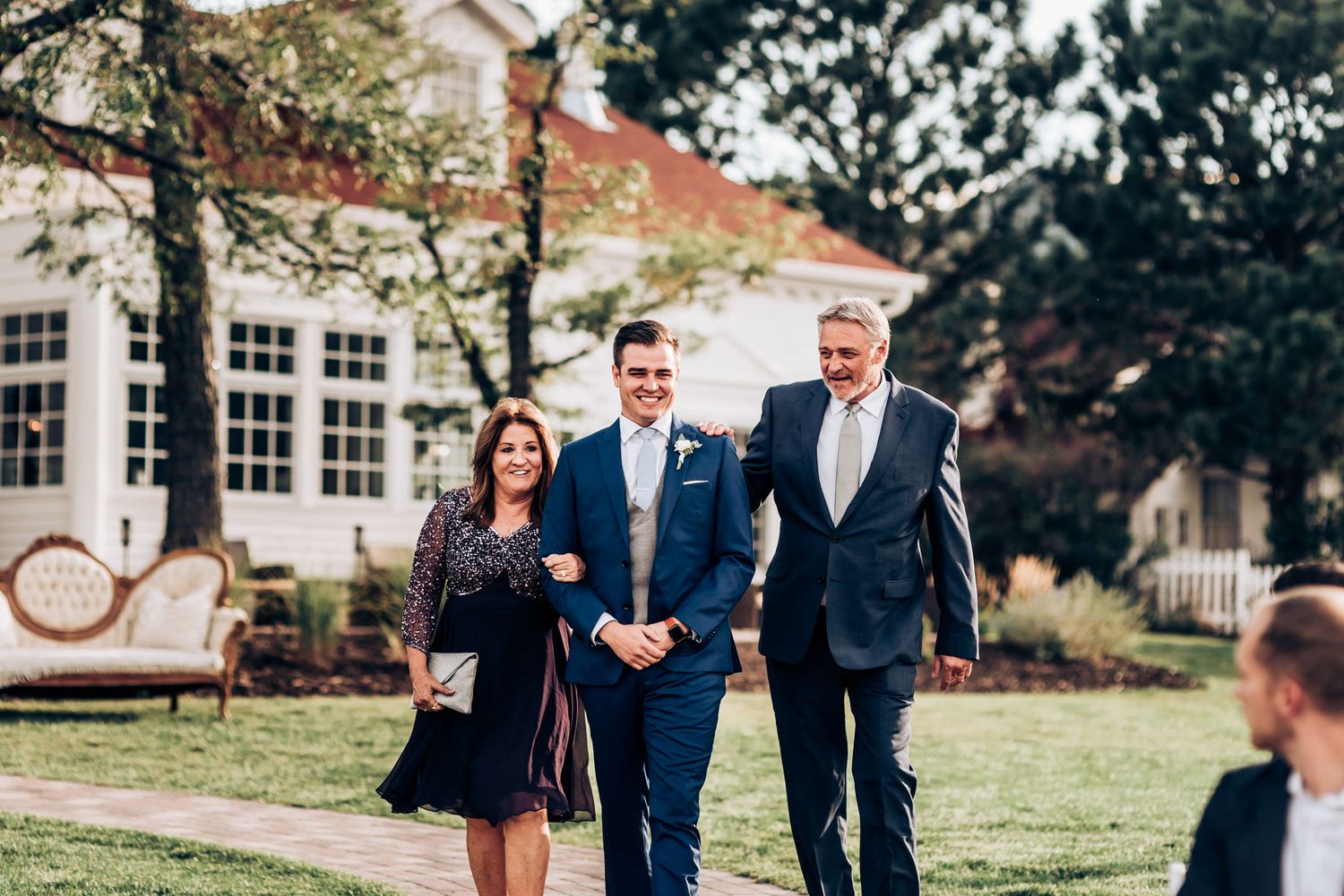 Wedding party members walking on grass path near elegant white building.