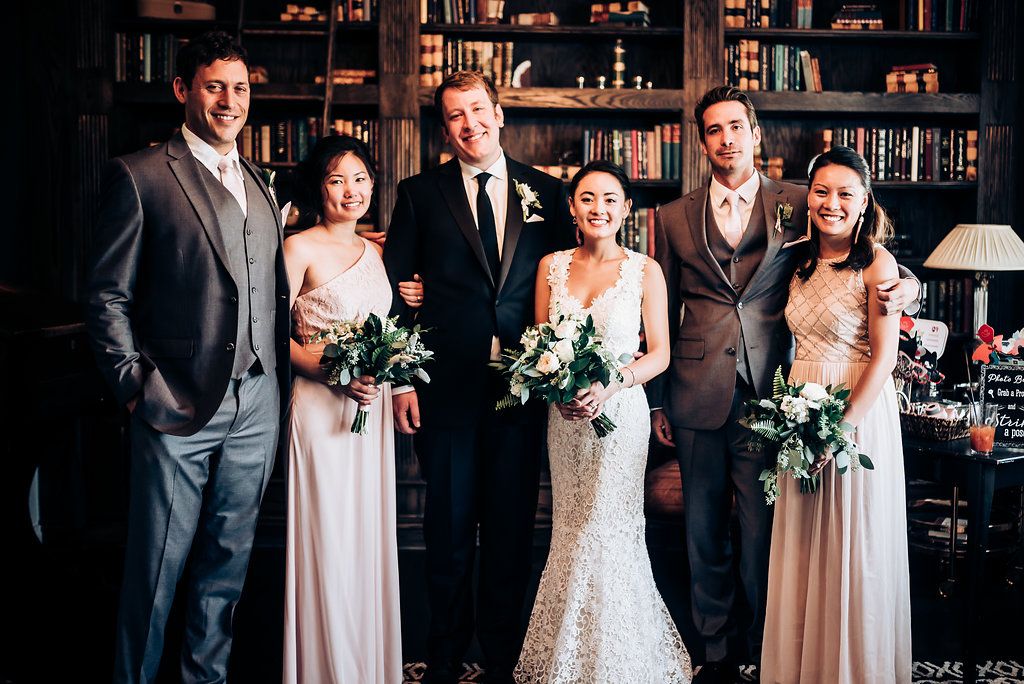 Wedding party members gather for formal portrait in front of classic library interior.