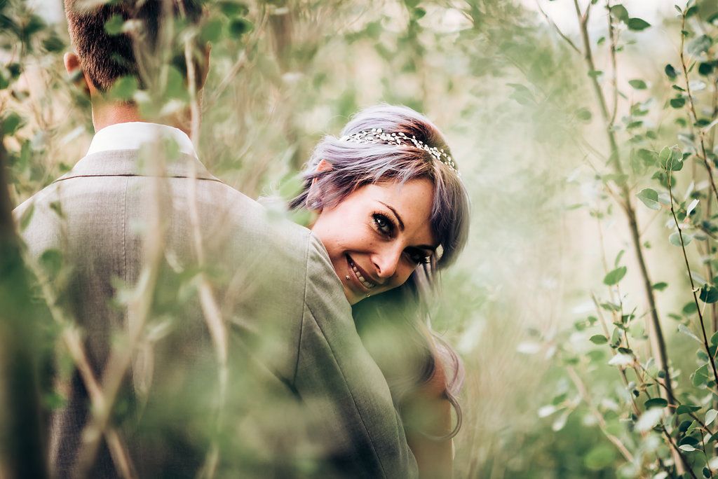 Candid bridal portrait through green foliage with delicate crystal headpiece.