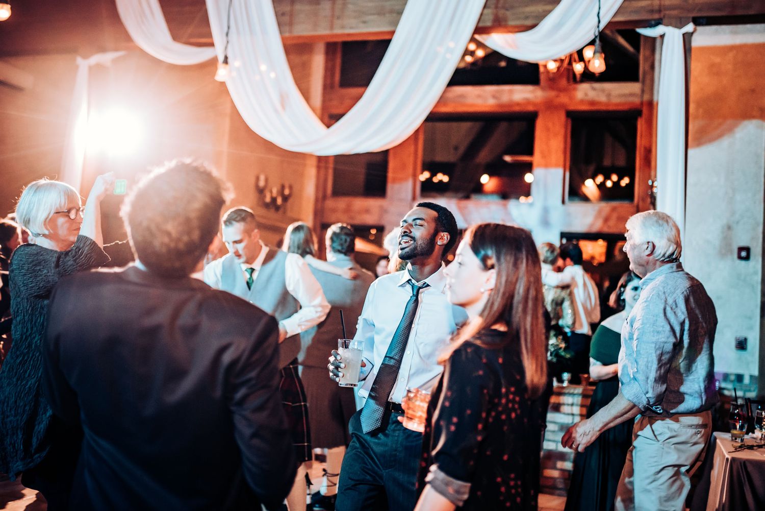 Wedding guests mingling and socializing under white ceiling drapes at an indoor reception.