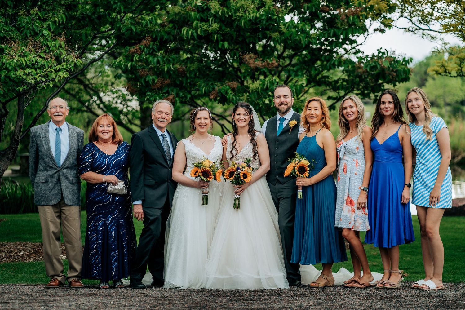 Wedding party and family members pose together outdoors in coordinated blue and formal attire.