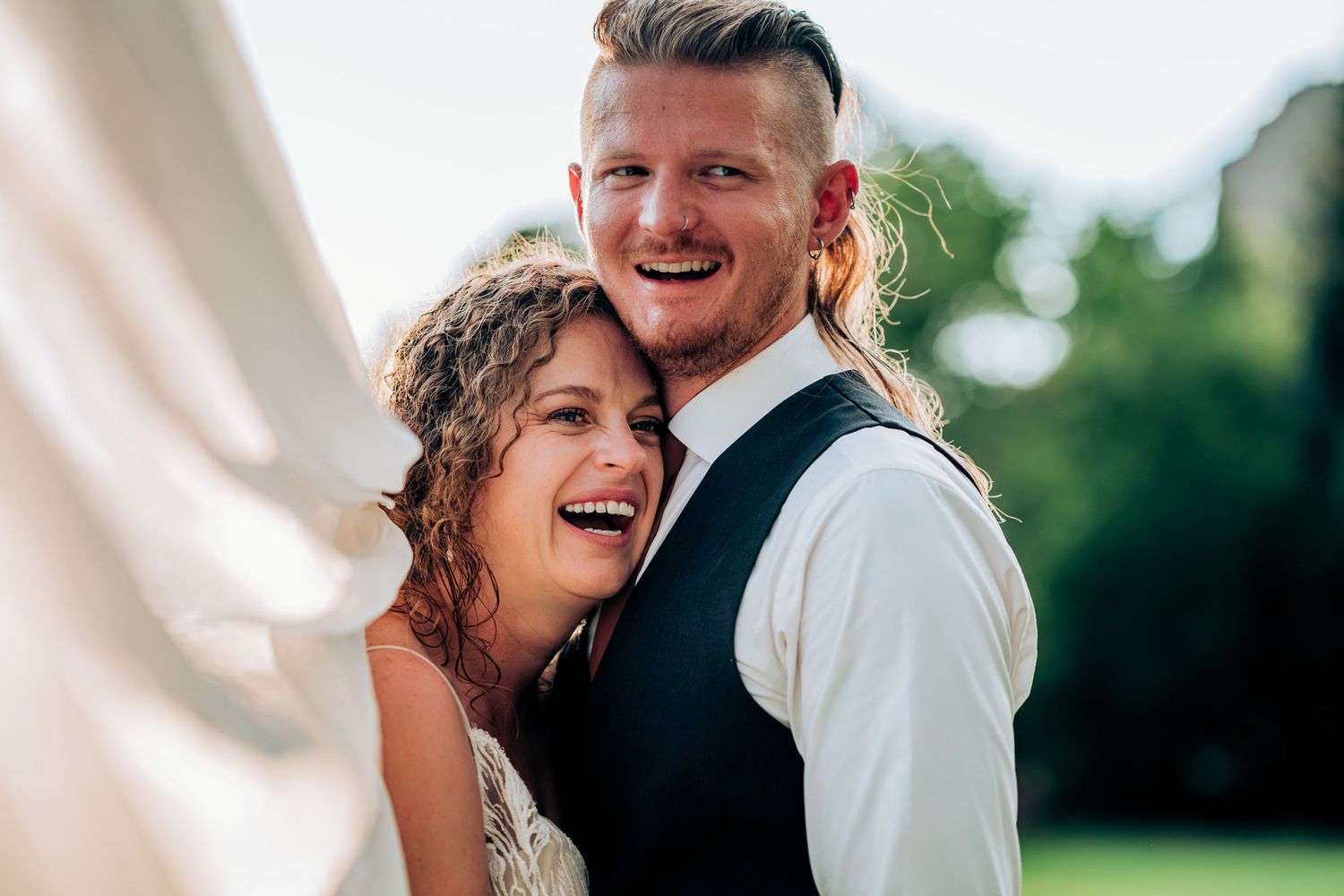 Happy newlyweds share joyful laughter in outdoor wedding portrait.