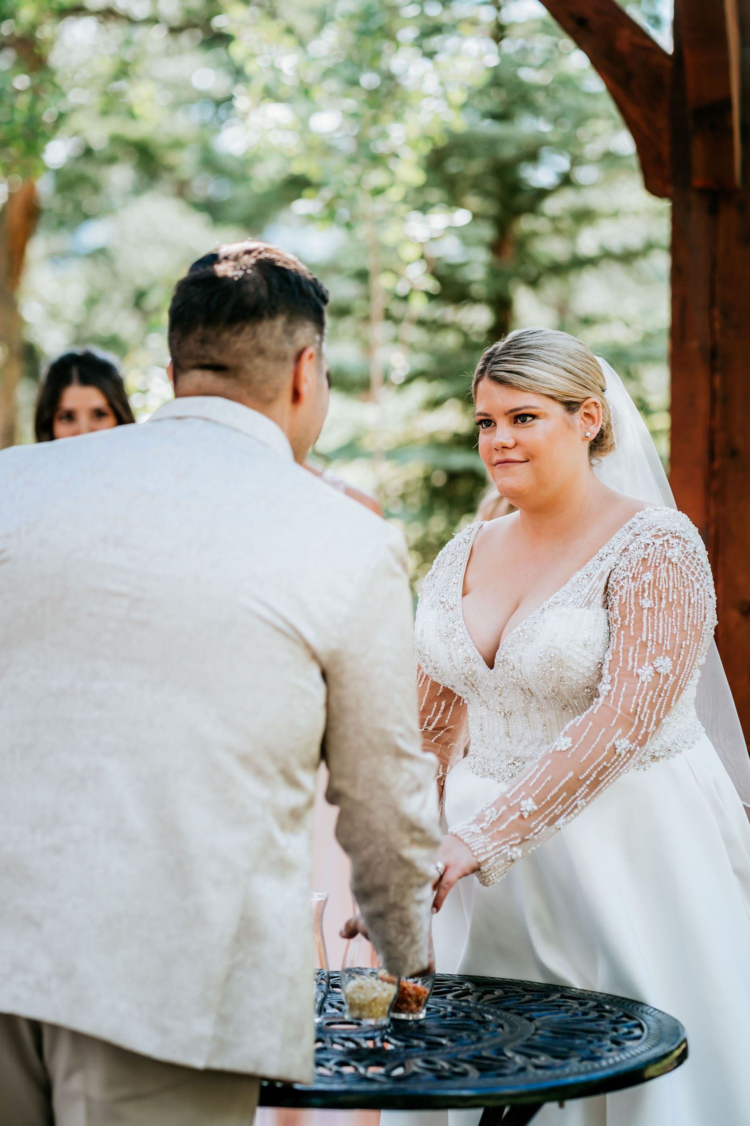 Wedding ceremony tablescape with couple exchanging vows under a wooden pavilion.