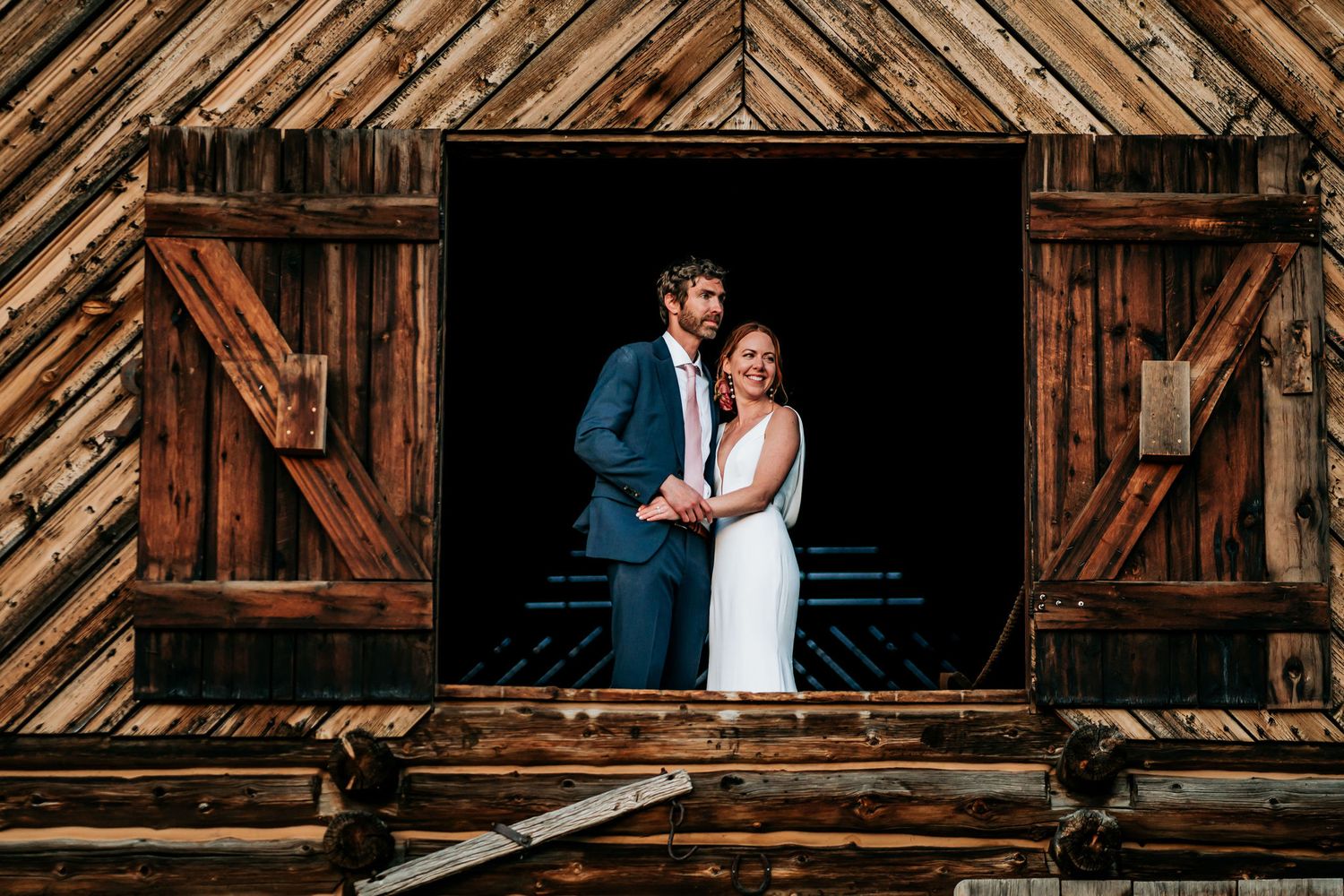 A couple poses in formal attire within the frame of a rustic barn doorway.
