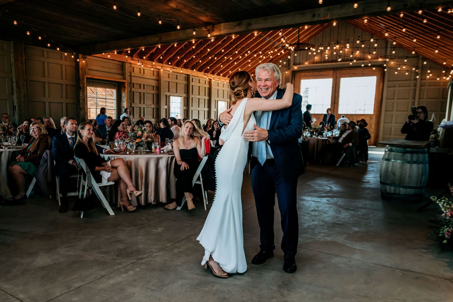 Dancing couples in a rustic barn venue decorated with string lights overhead.