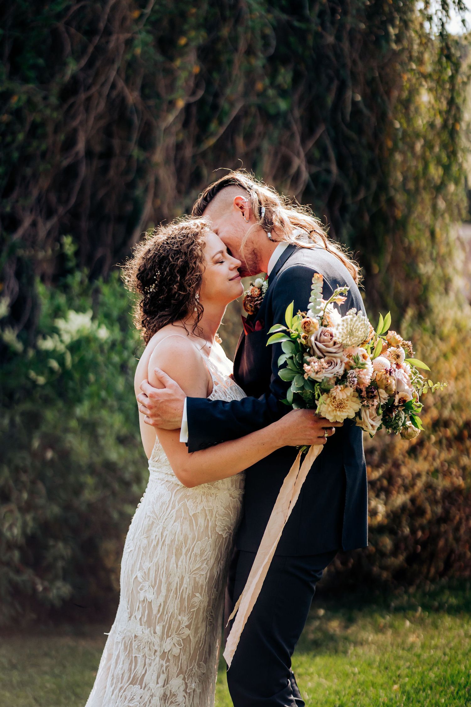 A joyful wedding couple embracing outdoors with a romantic floral bouquet.