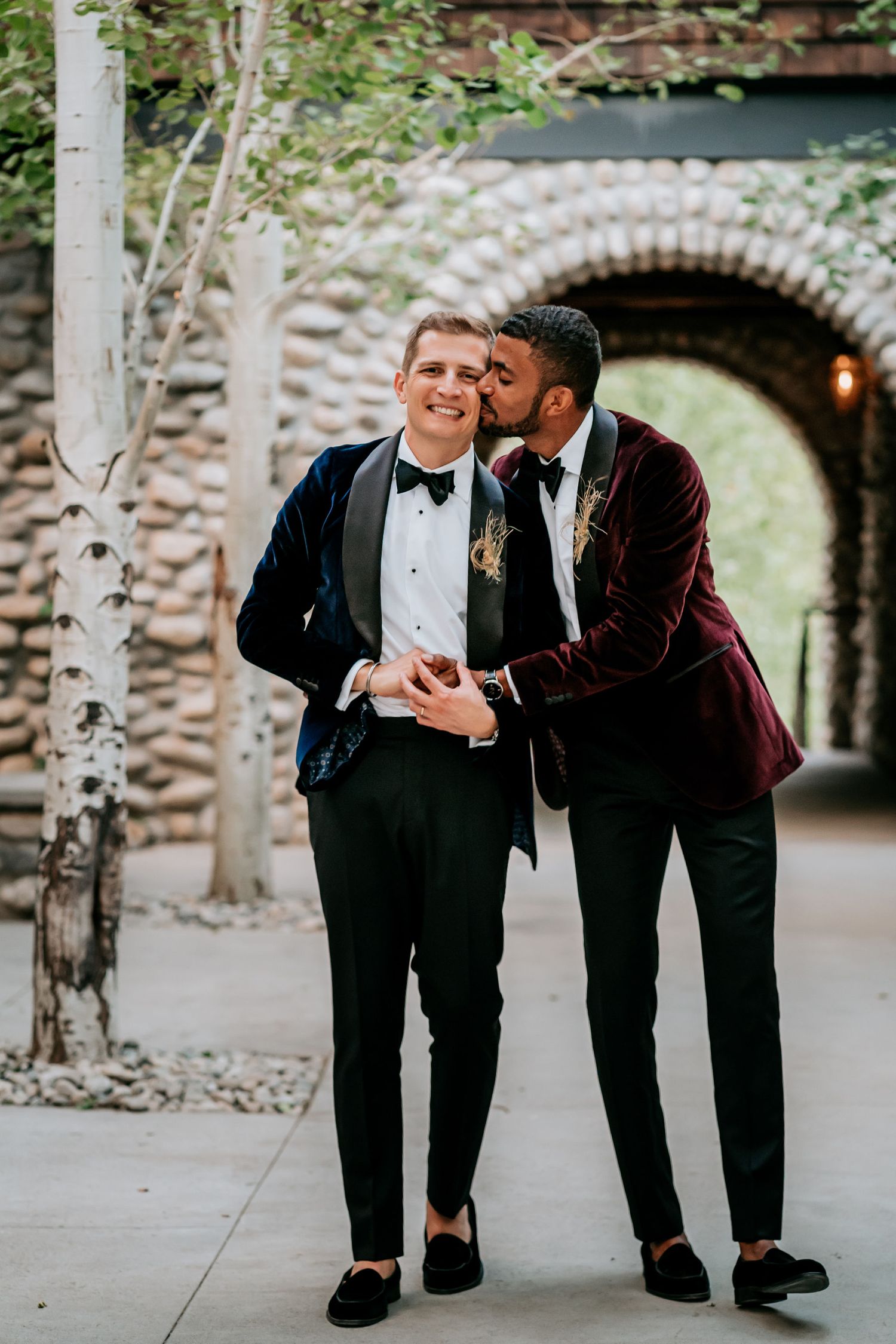 A romantic moment between two people in tuxedos under a stone archway.