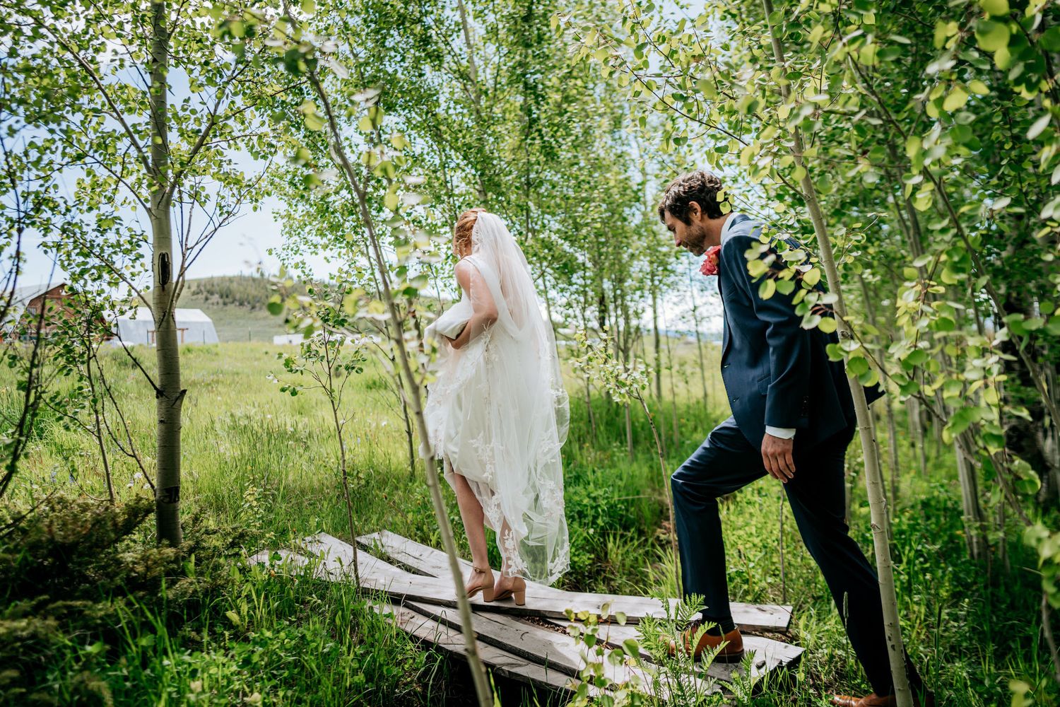Wedding couple walks playfully across a wooden boardwalk through an aspen grove.