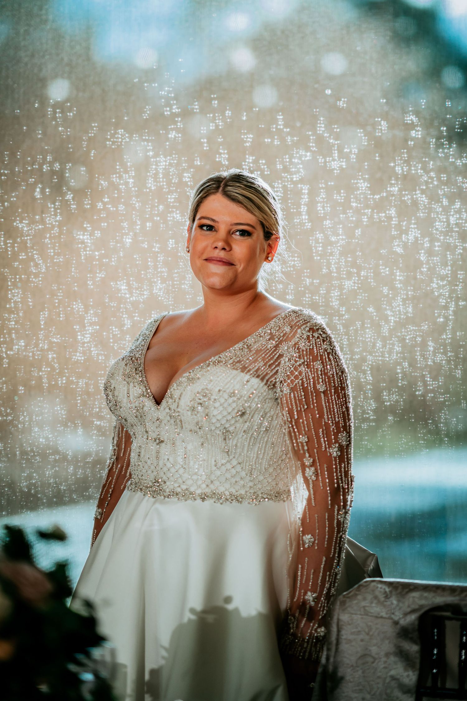 A bride in a beaded long sleeve wedding gown poses against a sparkling bokeh backdrop.