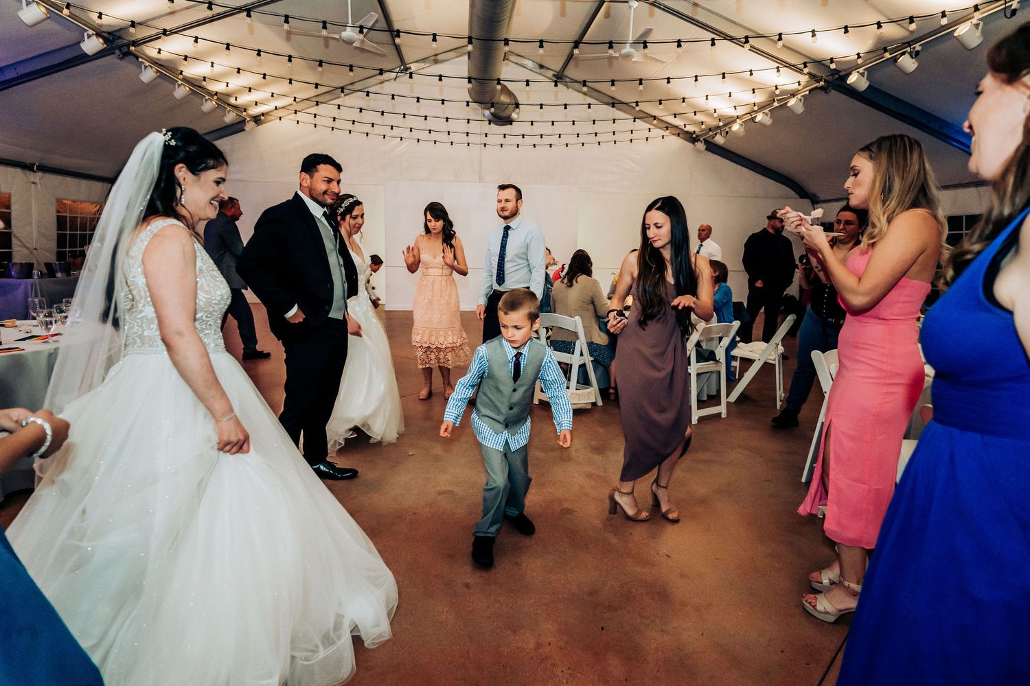 Wedding reception dance floor with guests celebrating under string lights.