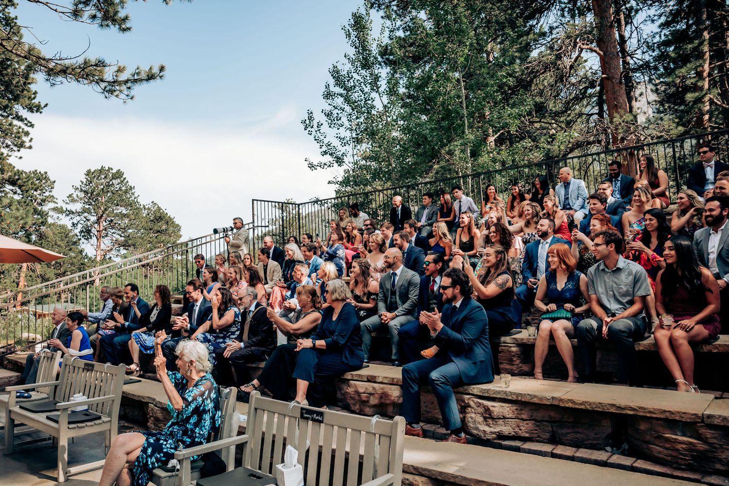Wedding guests seated on wooden benches in a forest amphitheater.