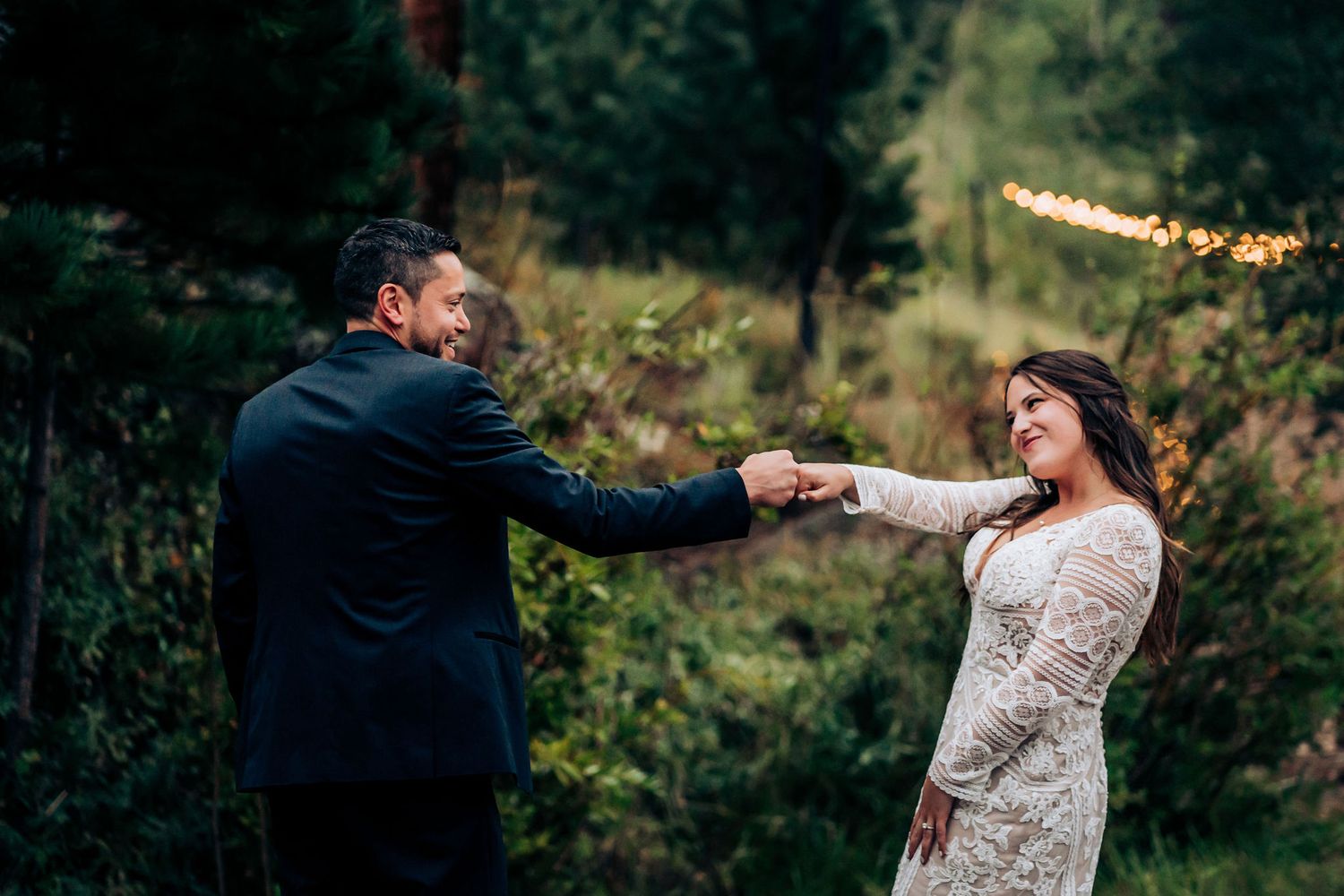 Couple in wedding attire dancing playfully on a stone pathway surrounded by nature.