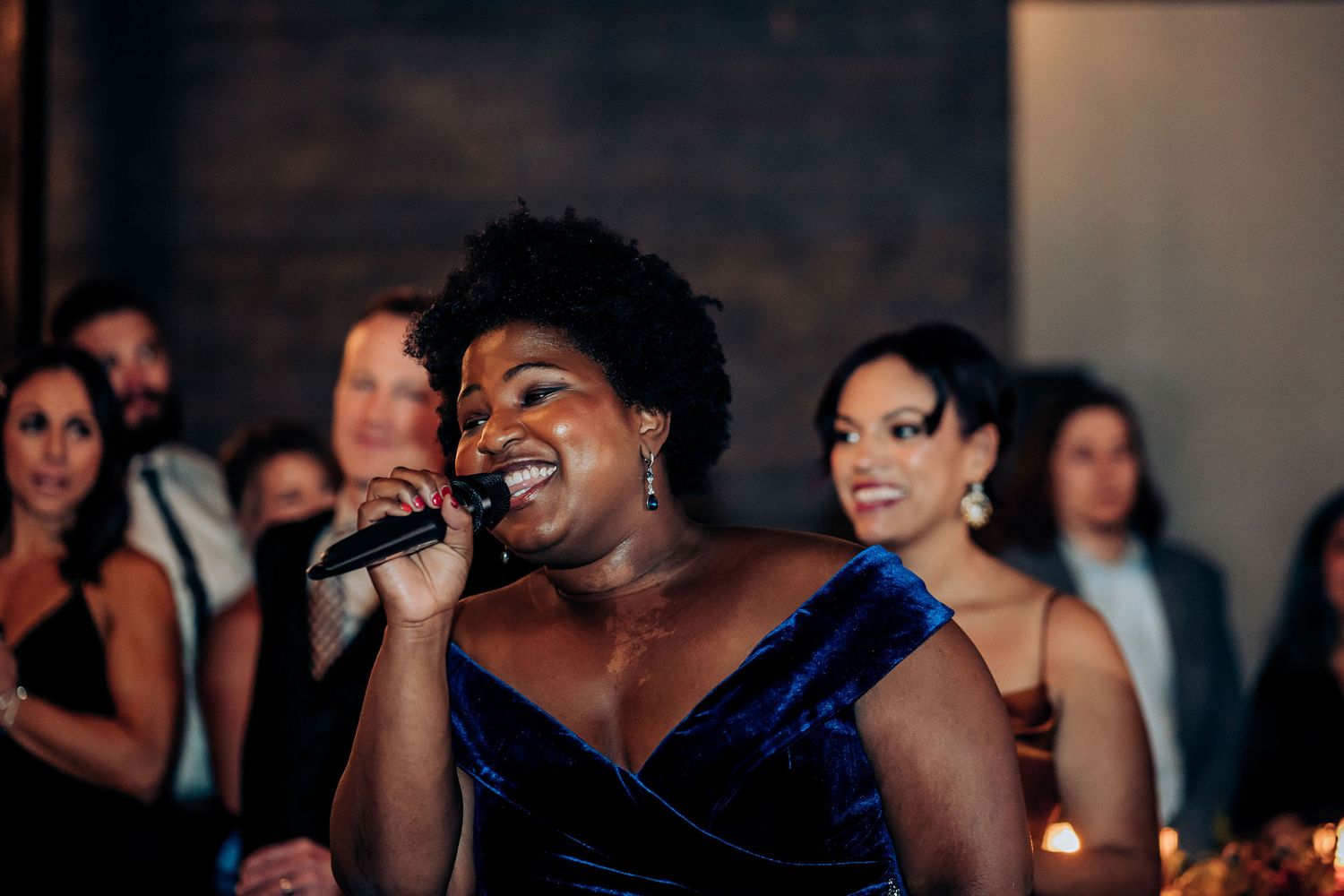 Singer in a deep blue velvet dress performs passionately at an elegant evening event.