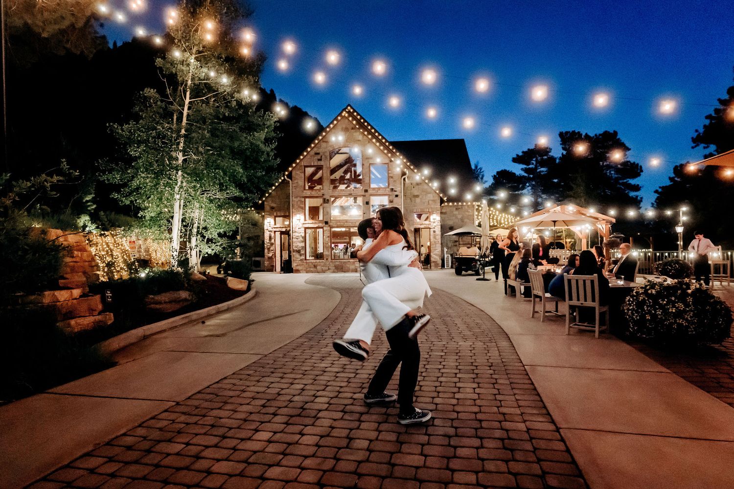 Dancing under string lights outside a rustic barn venue on a romantic evening.