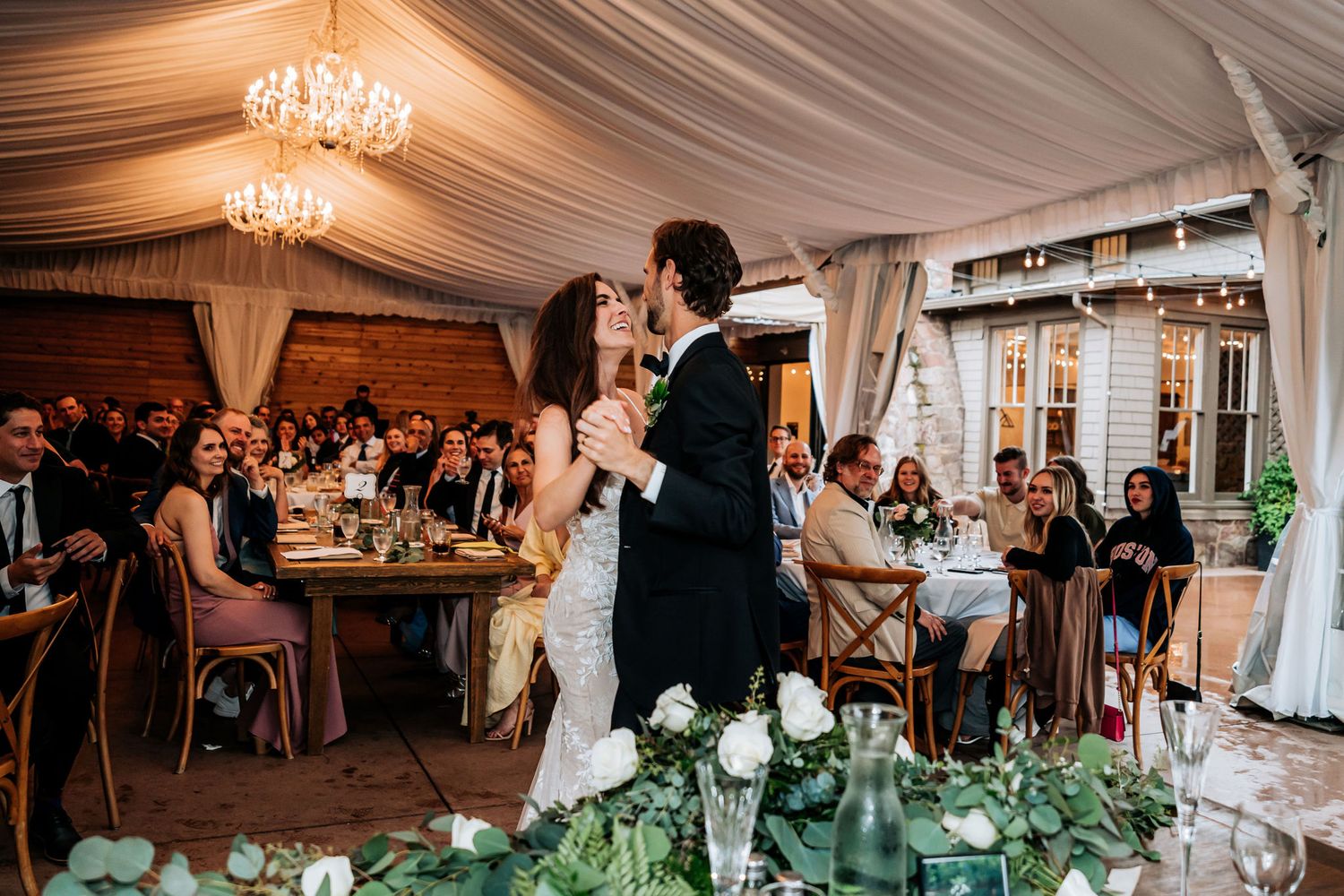 A wedding reception in an elegant tented venue with crystal chandeliers and draped fabric.