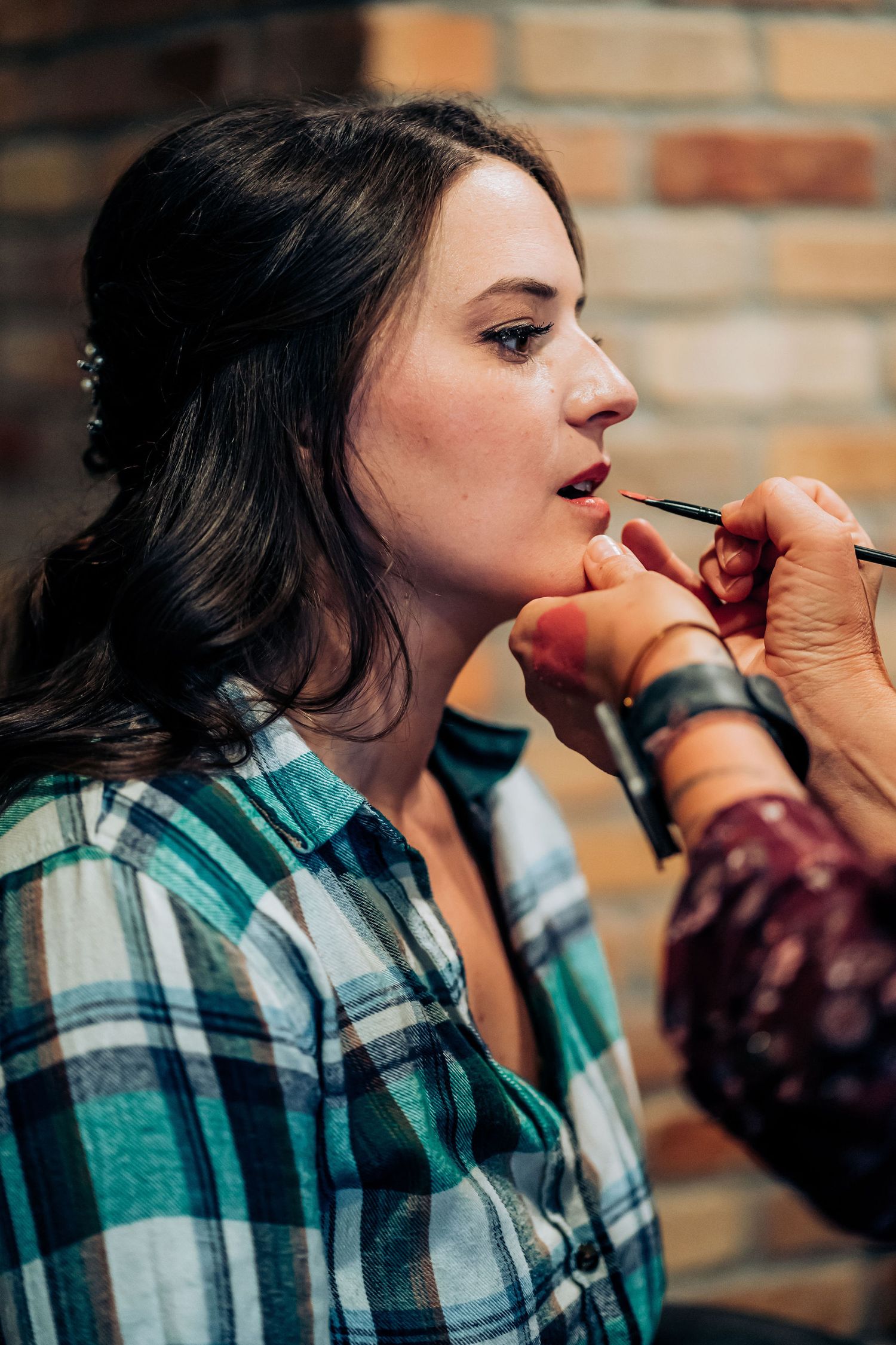 Professional makeup application in progress against brick wall backdrop.