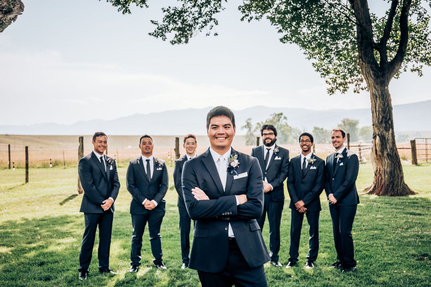Formal groomsmen group photo on grass with mountain landscape behind them.