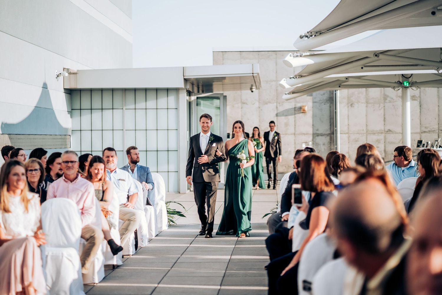 An elegant rooftop wedding ceremony with guests seated in white chairs under modern architectural canopies.