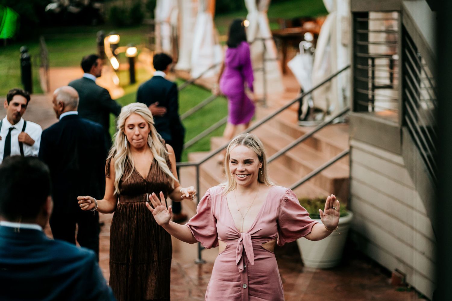 Wedding guests dancing and celebrating outdoors on a garden patio at dusk.