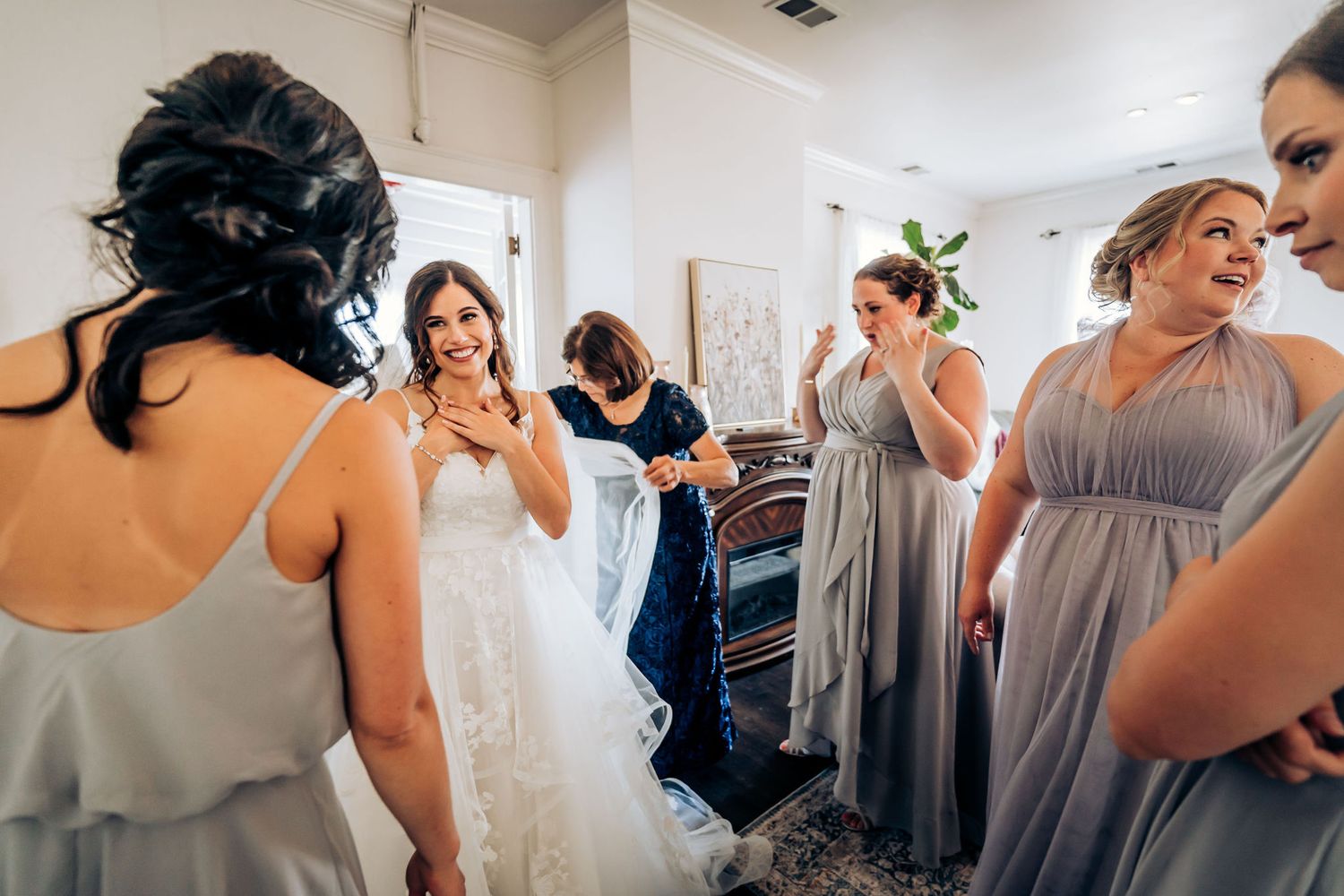 Bridesmaids in grey dresses gather around the bride during wedding preparations.
