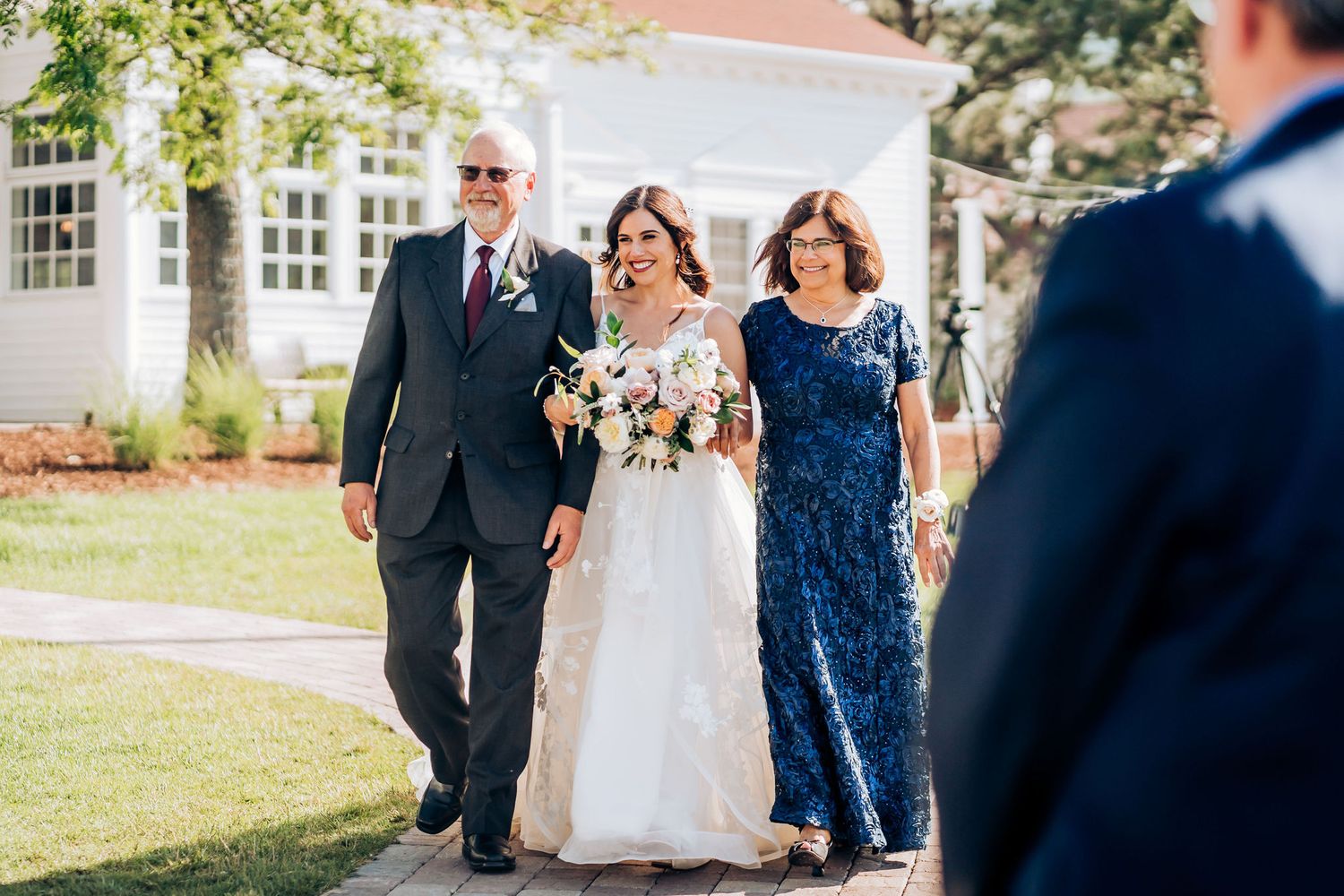 Wedding party walks down outdoor pathway during ceremony entrance.