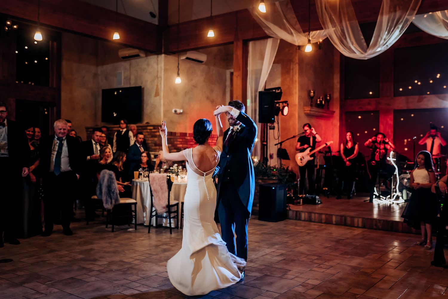 A elegant wedding dance under warm lighting in a rustic venue with draped fabric decor.