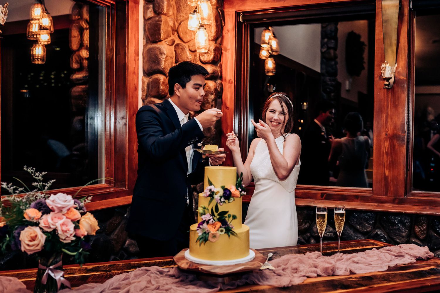 Newlyweds sharing a playful moment while cutting their yellow floral wedding cake.