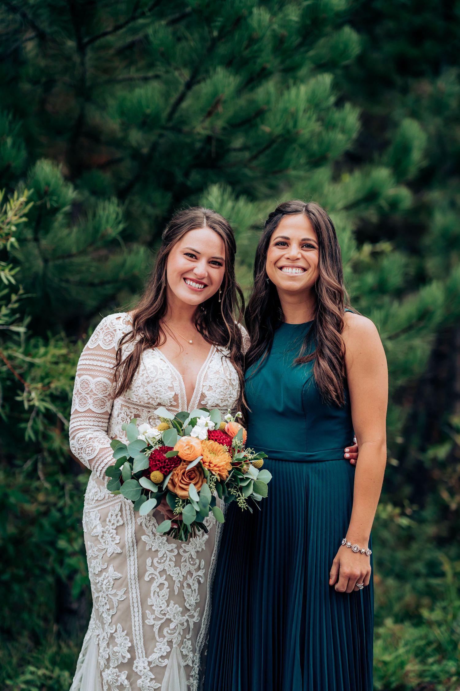 A bride and bridesmaid in contrasting white and teal dresses pose with colorful bouquets.