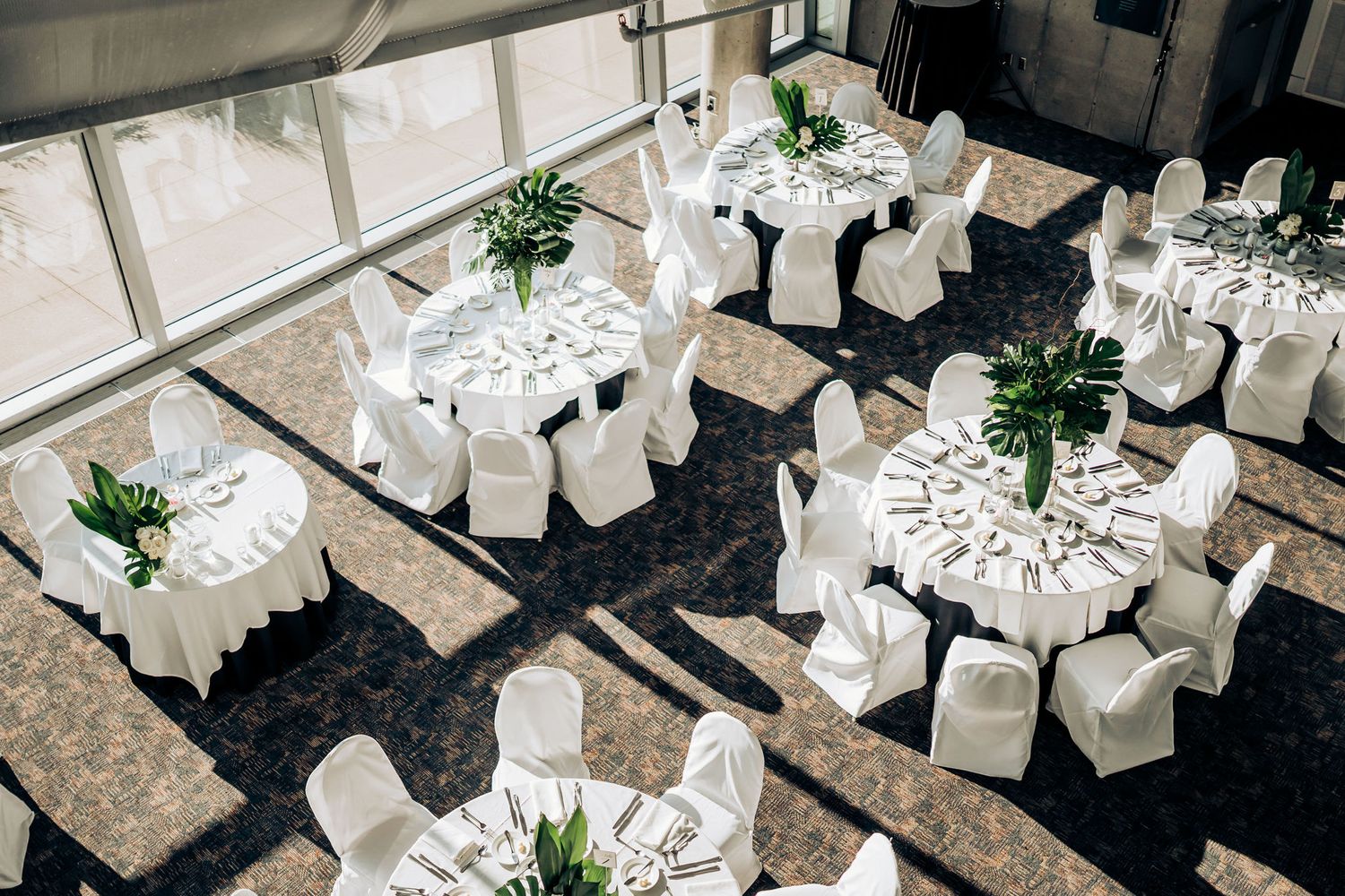 An elegant wedding reception venue with round tables, white chair covers, and green centerpieces viewed from above.
