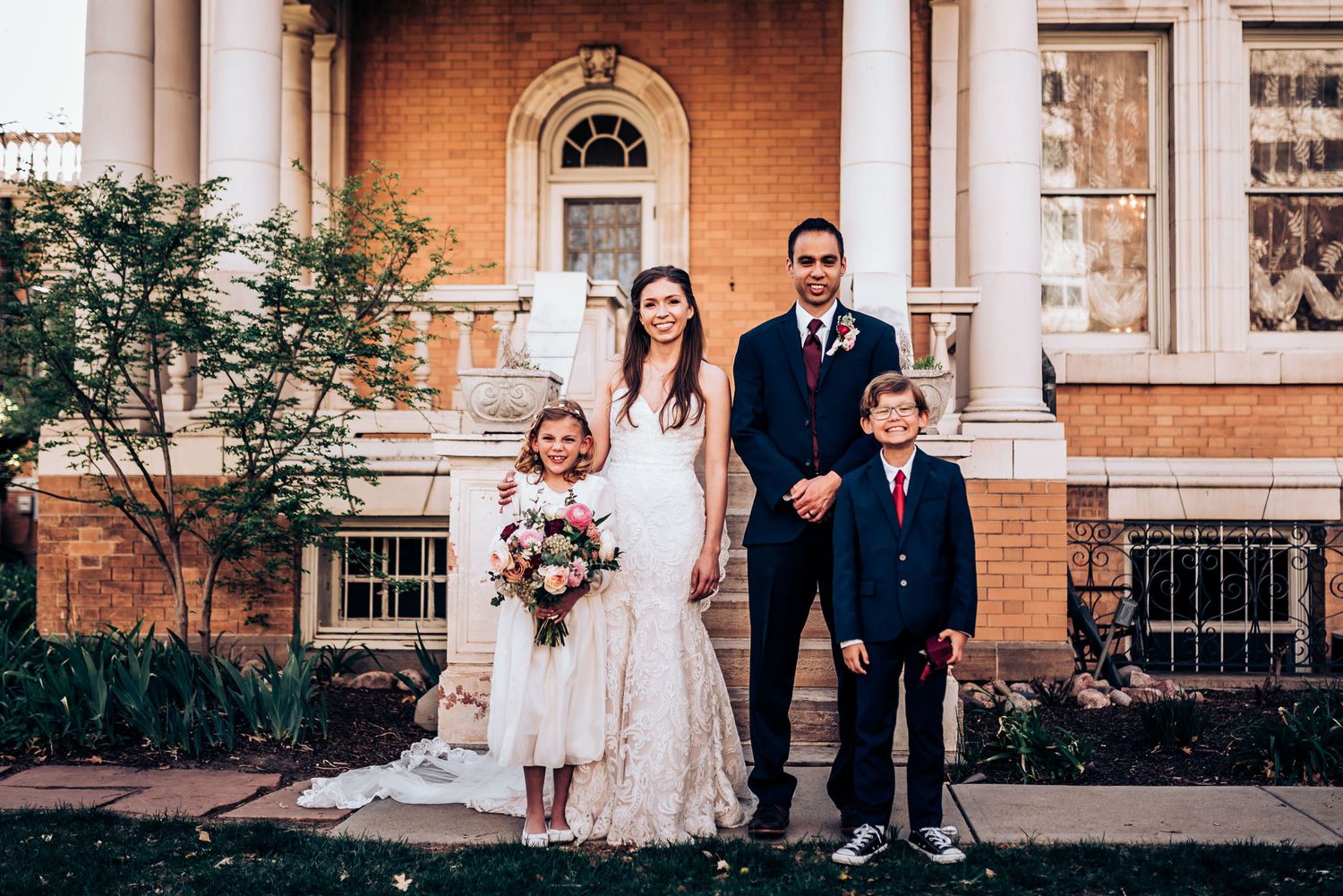 Wedding portrait with flower girl and young attendant outside brick colonial building.