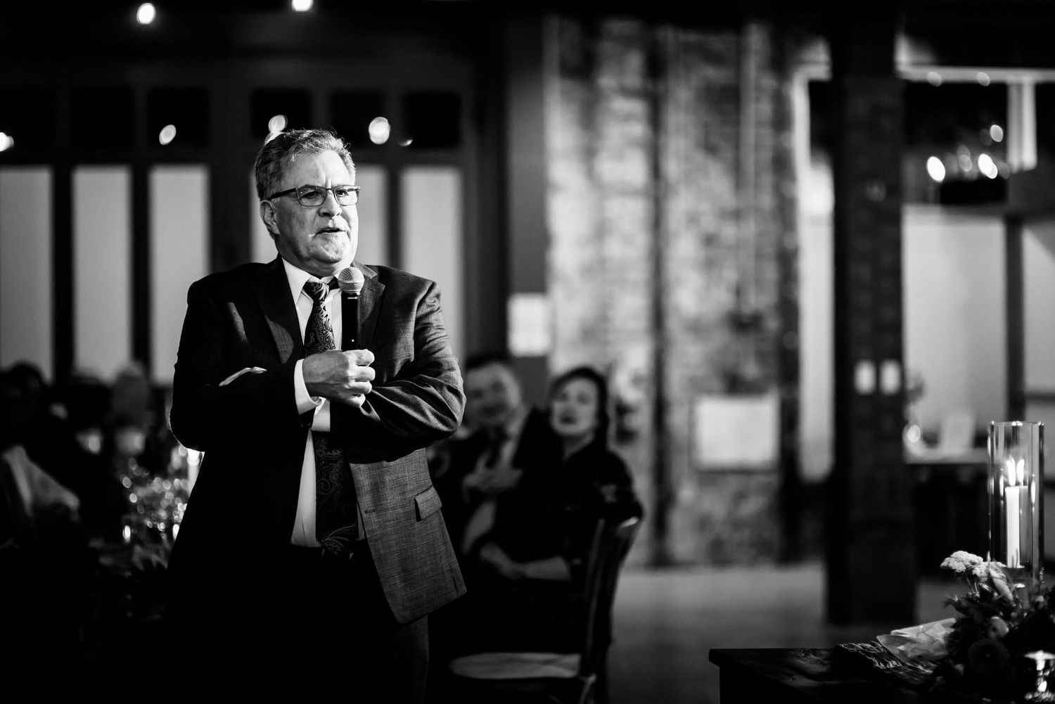 A speaker addresses an audience in a dramatic black and white shot with exposed brick backdrop.