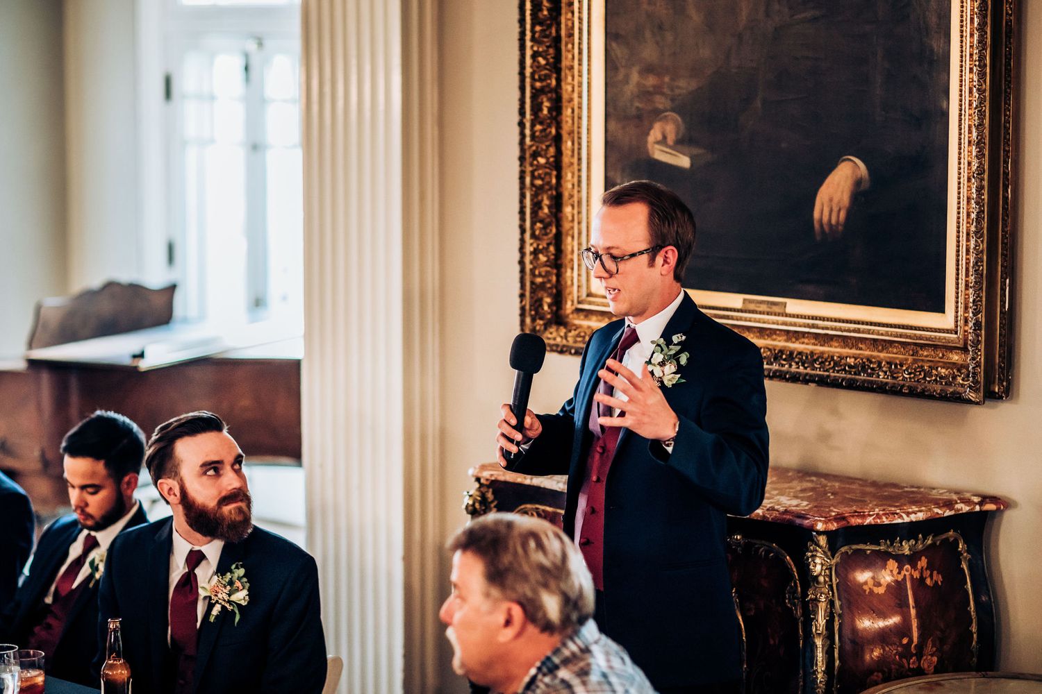 Wedding speech being delivered in an elegant room with classical portrait backdrop.