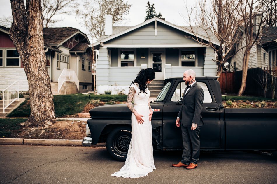Wedding couple poses with vintage pickup truck outside suburban home.