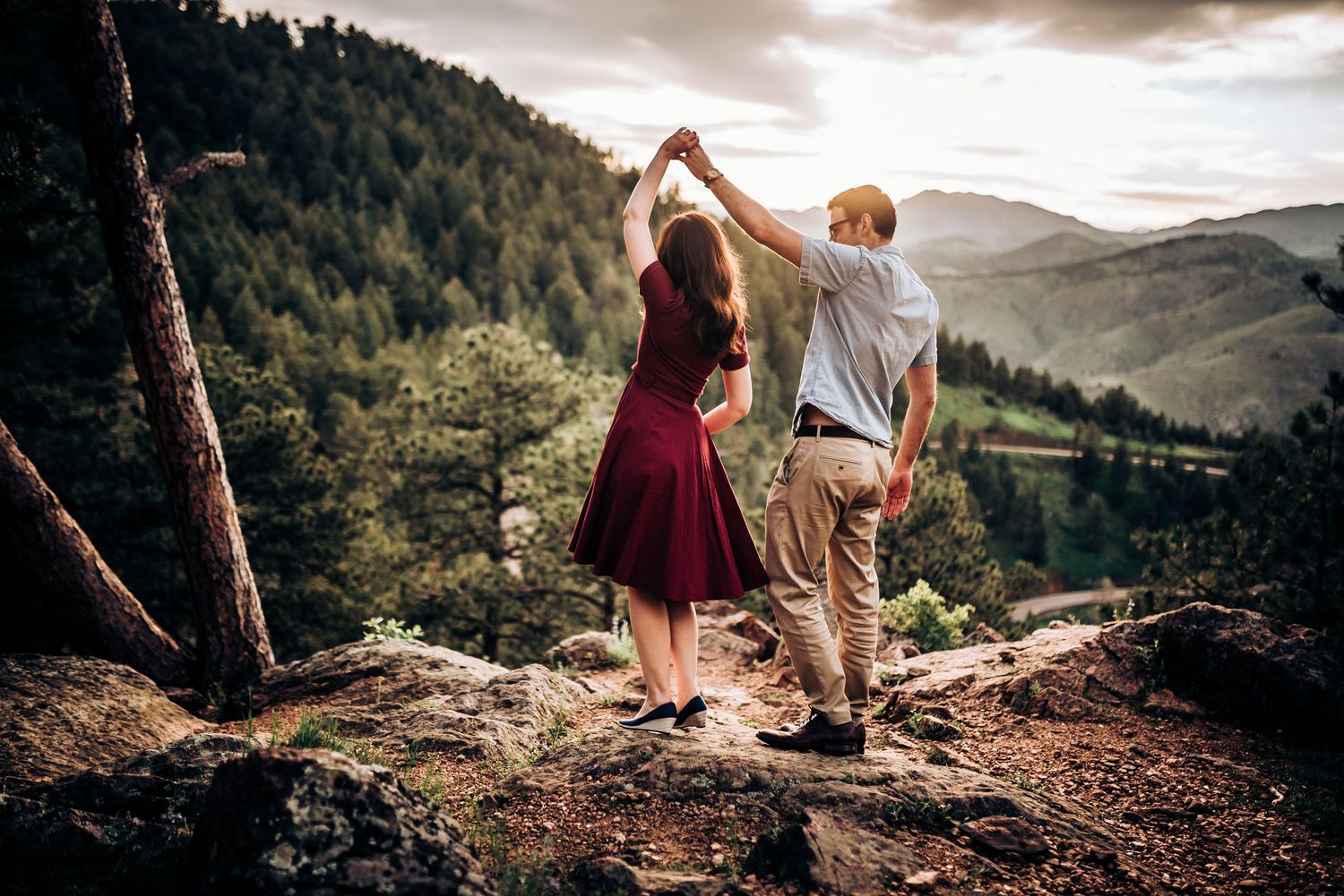 Couple dancing together on mountain overlook with expansive valley view behind them.