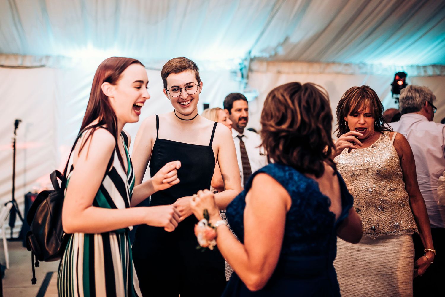 Wedding guests share laughs and dance together at an indoor reception with ambient lighting.