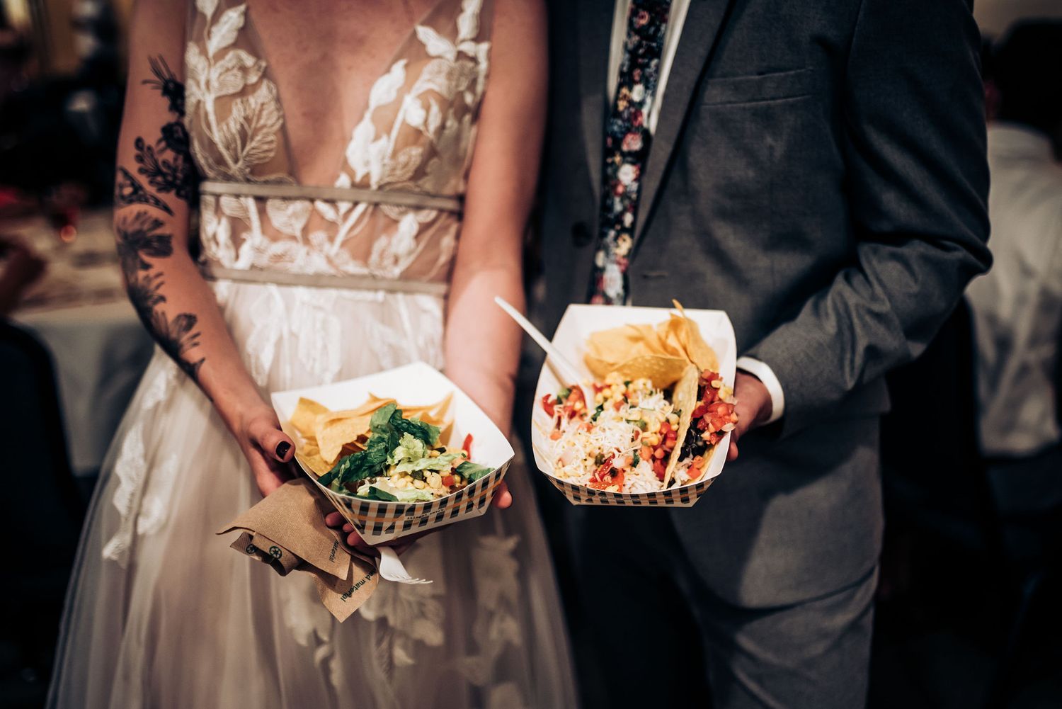 Wedding couple holding casual food dishes at a reception under string lights.