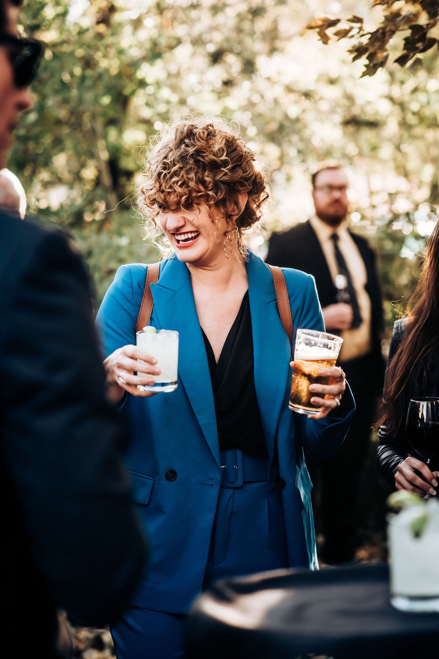 Wedding guest in bright blue blazer enjoying cocktails at outdoor reception.