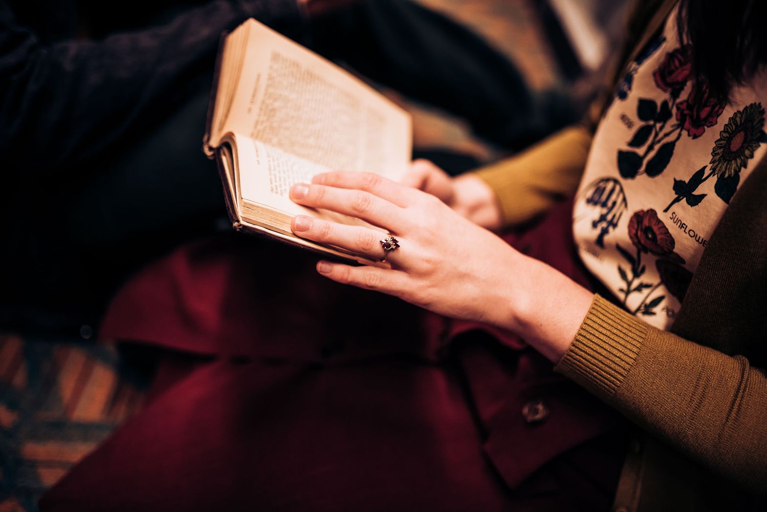 Hands hold open a book while reading in warm lighting.