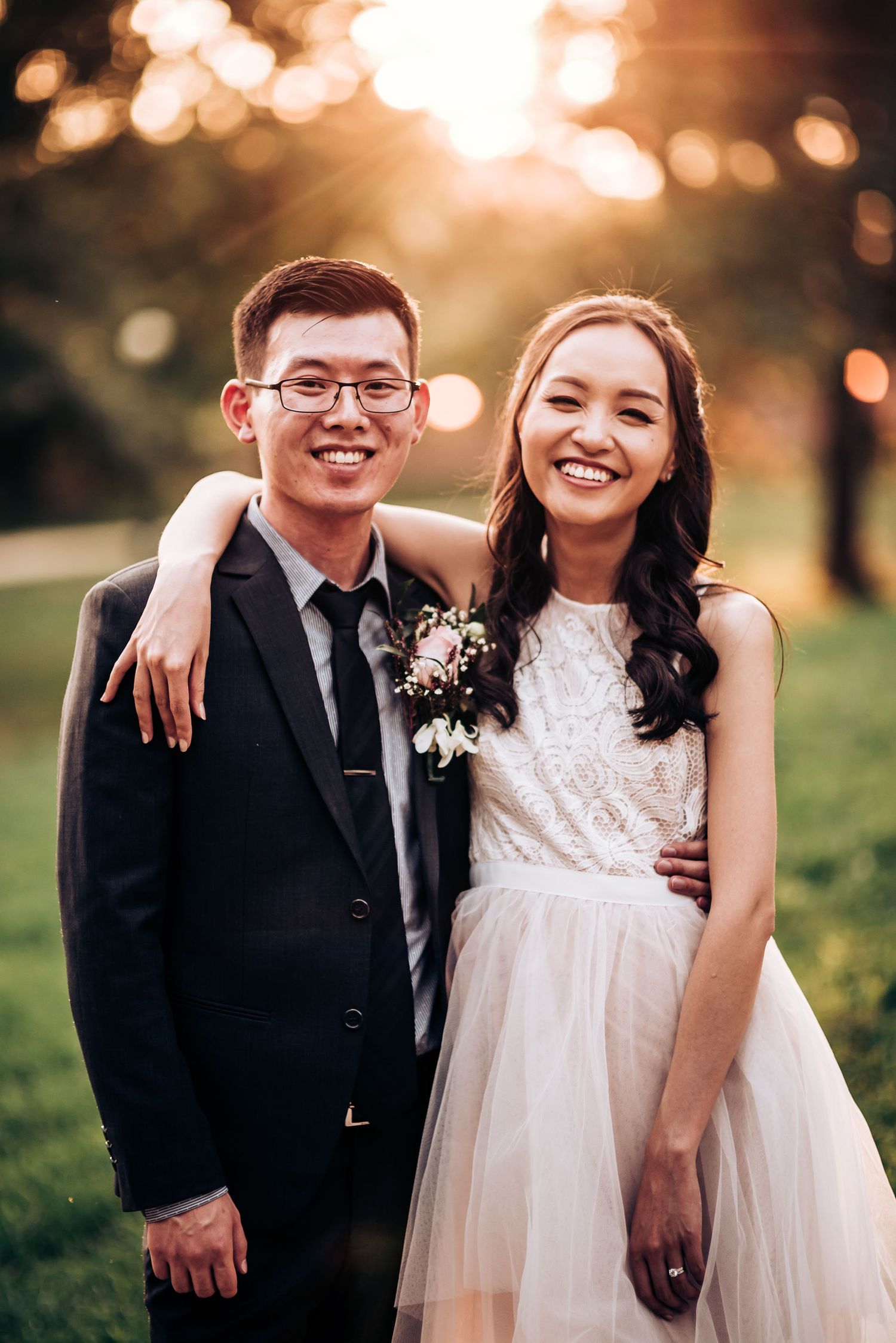 A wedding couple poses together outdoors during golden hour with natural bokeh lighting.