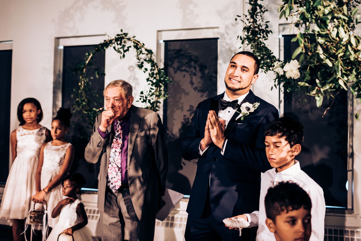 Guests share emotional reactions during wedding speeches beneath decorative greenery.
