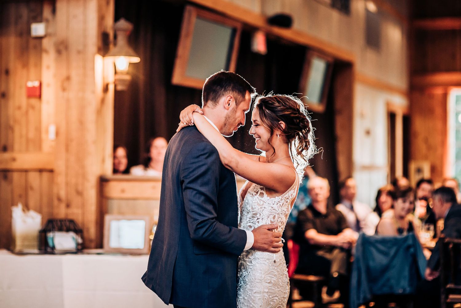 A couple shares their first dance at their rustic barn wedding reception with warm lighting and wooden beams.
