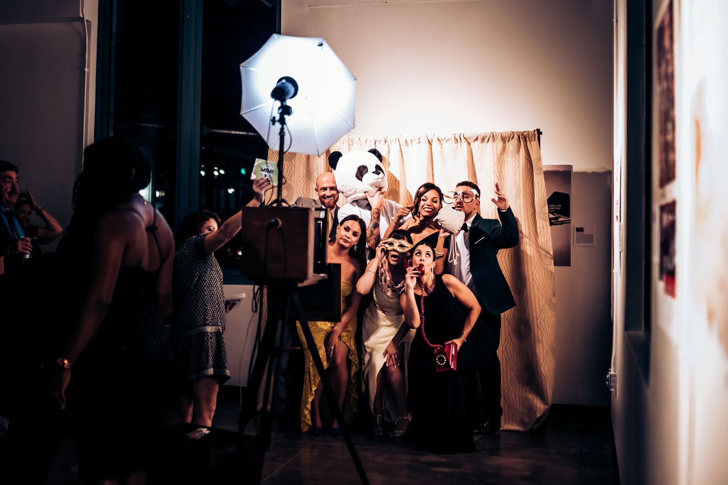 A lively wedding party poses together in front of studio lighting equipment at a reception venue.