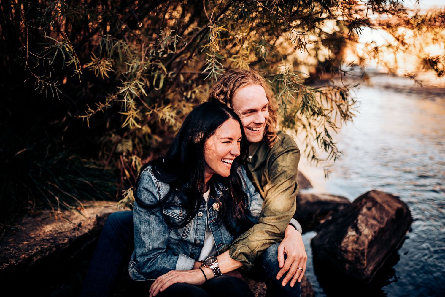 Couple shares lighthearted moment while sitting by waterfront during sunset.